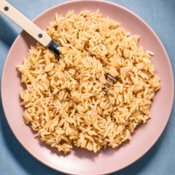 Rice with chicken broth and butter served on a pink plate with a fork, showing fluffy long-grain rice cooked in savory chicken broth and butter.
