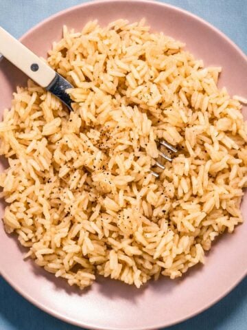 Rice with chicken broth and butter served on a pink plate with a fork, showing fluffy long-grain rice cooked in savory chicken broth and butter.