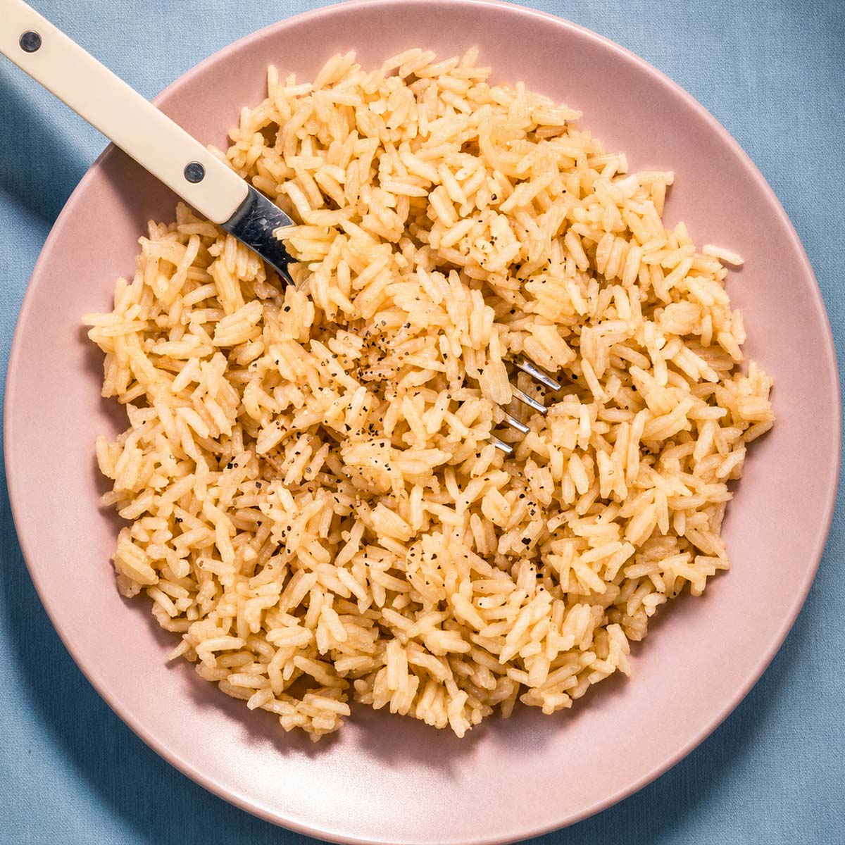 Rice with chicken broth and butter served on a pink plate with a fork, showing fluffy long-grain rice cooked in savory chicken broth and butter.