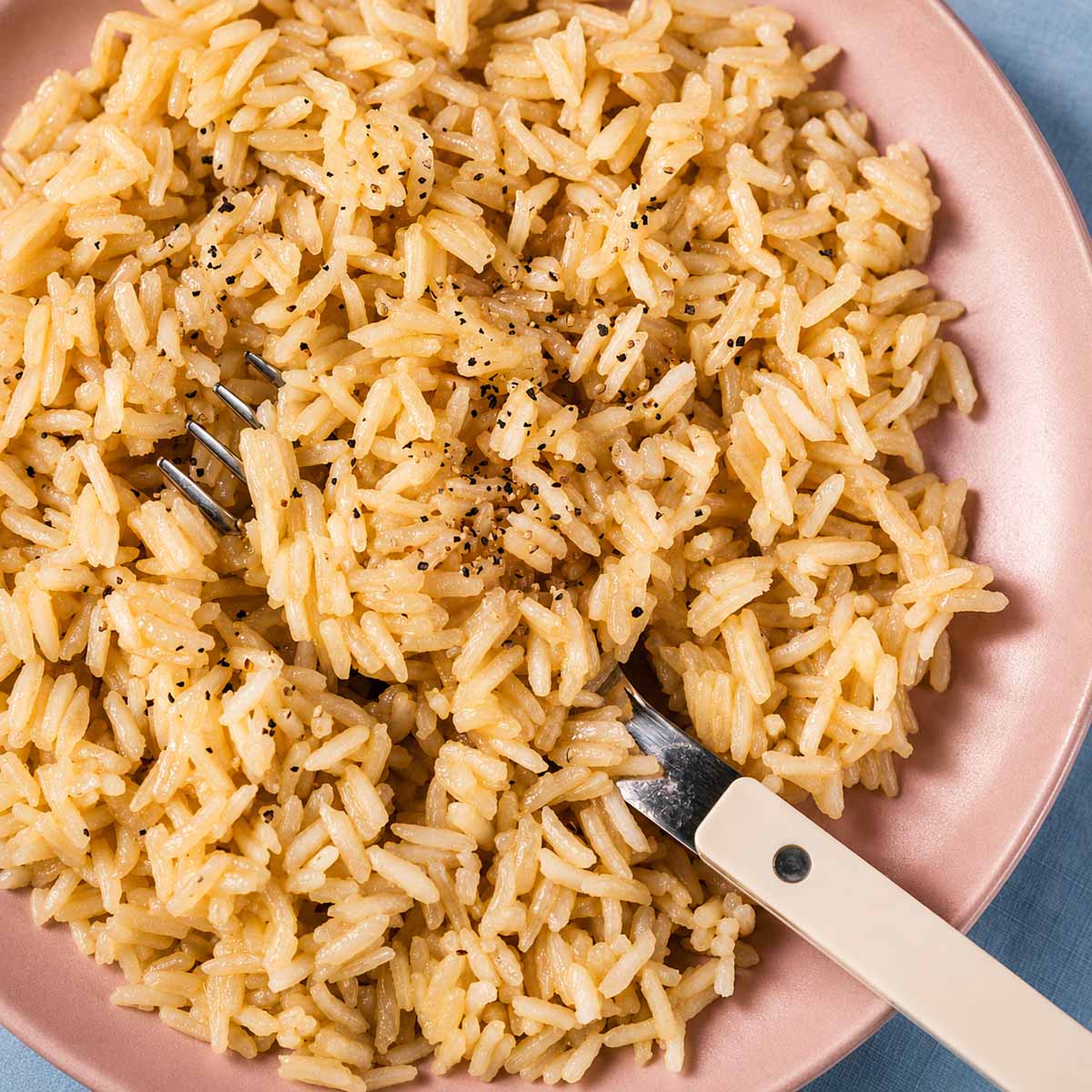 Rice with chicken broth and butter served on a pink plate with a fork, showing fluffy long-grain rice cooked in savory chicken broth and butter.