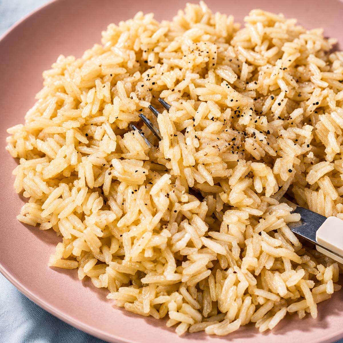 Rice with chicken broth and butter served on a pink plate with a fork, showing fluffy long-grain rice cooked in savory chicken broth and butter.