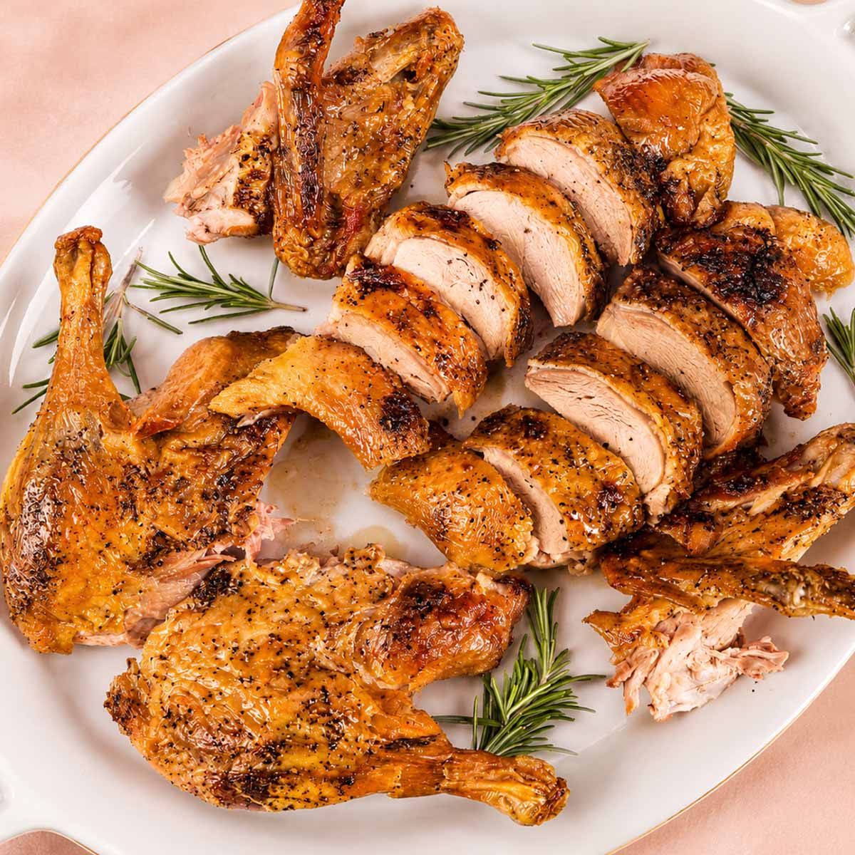 Roasted duck carved into slices and pieces on a white platter, showing juicy meat and crisp golden skin, garnished with fresh rosemary sprigs.
