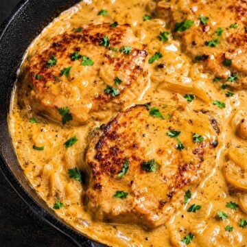 Smothered pork chops in creamy onion gravy with fresh parsley in a cast-iron skillet