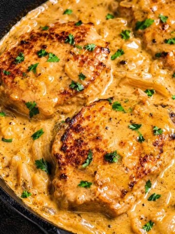 Smothered pork chops in creamy onion gravy with fresh parsley in a cast-iron skillet