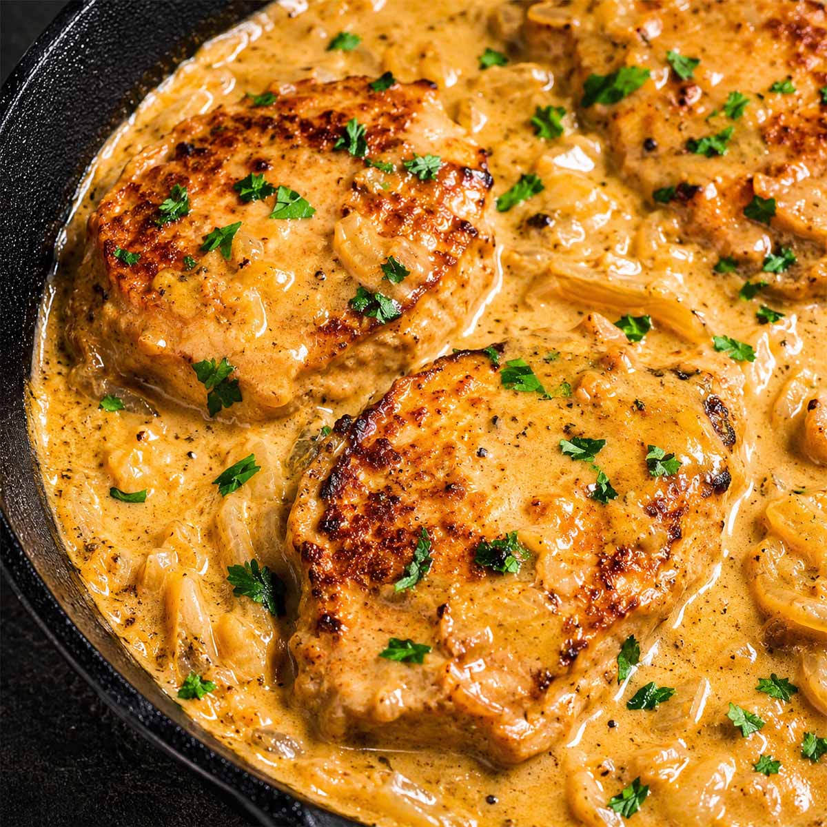 Smothered pork chops in creamy onion gravy with fresh parsley in a cast-iron skillet