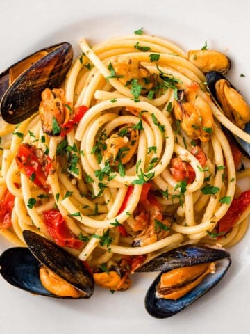 Spaghetti with mussels in a garlic and parsley sauce with cherry tomatoes, classic Italian seafood pasta on a white plate.