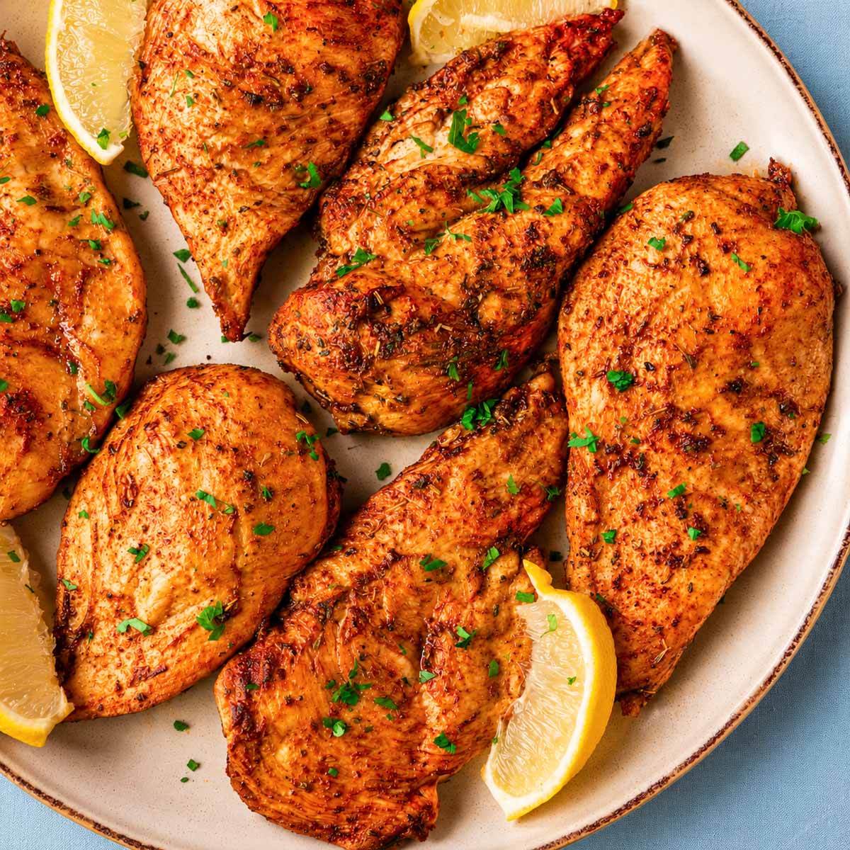 Thin sliced chicken breast in the oven arranged on a serving platter with golden edges, chopped parsley, and fresh lemon wedges.