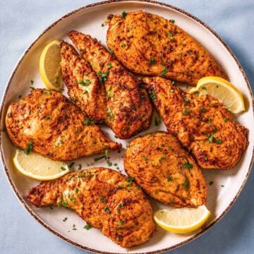 Thin sliced chicken breast in the oven baked until juicy and golden, served with fresh parsley and lemon wedges on a ceramic platter.