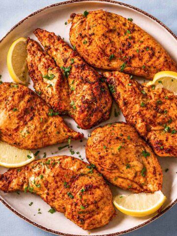 Thin sliced chicken breast in the oven baked until juicy and golden, served with fresh parsley and lemon wedges on a ceramic platter.