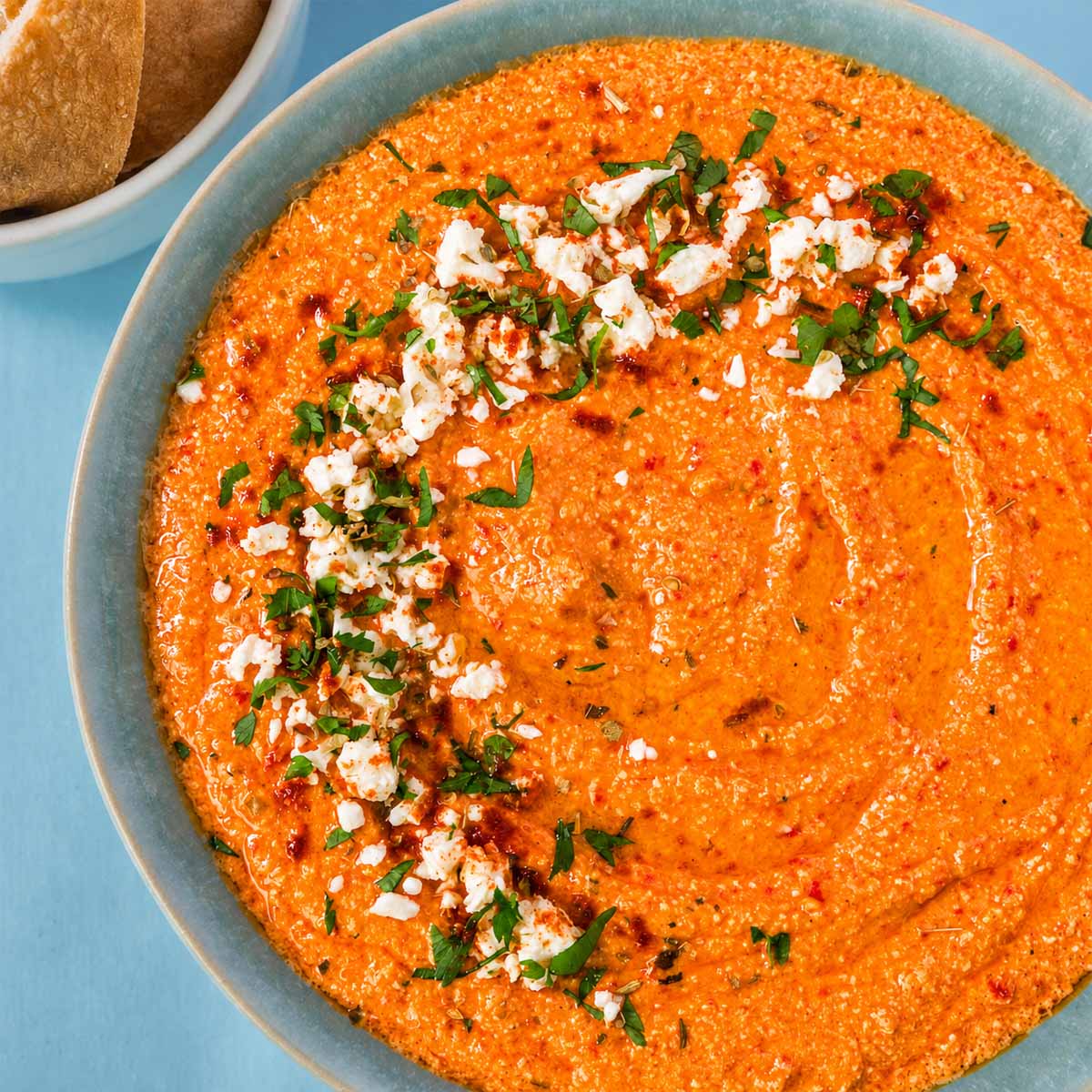 Creamy tirokafteri Greek spicy feta dip topped with crumbled feta, chopped parsley, and olive oil, served in a blue bowl.