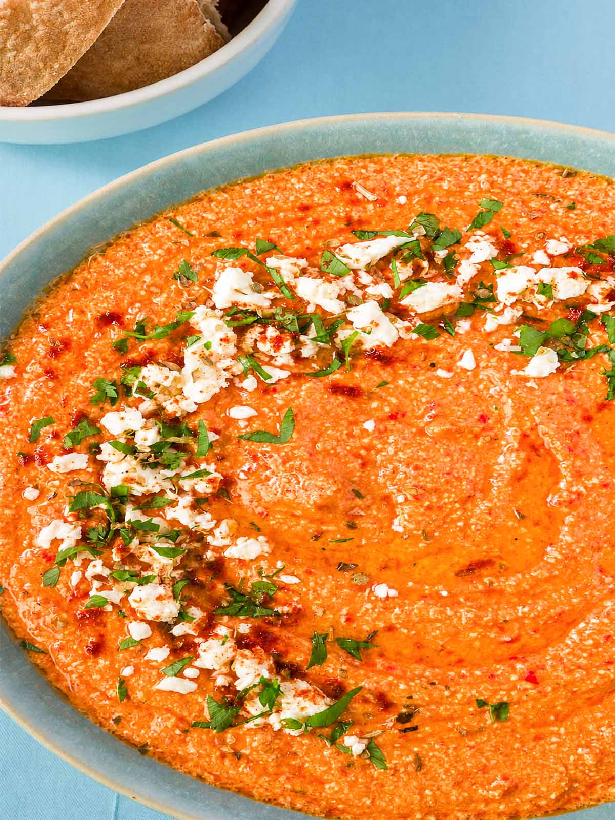 Close-up of tirokafteri Greek spicy feta dip with a swirled top, finished with crumbled feta and chopped parsley in a blue bowl.