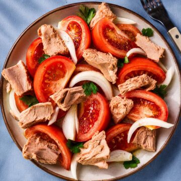 Spanish tuna salad with tomatoes, sliced onion, and parsley served on a ceramic plate with olive oil