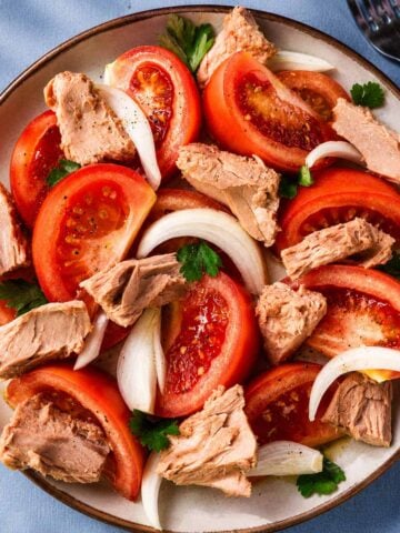 Spanish tuna salad with tomatoes, sliced onion, and parsley served on a ceramic plate with olive oil
