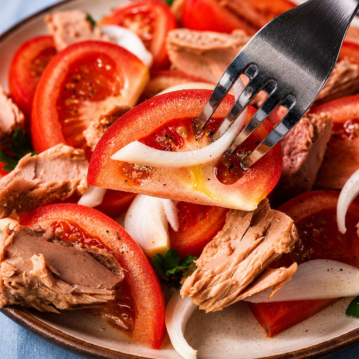 Fork lifting a tomato slice from Spanish tuna salad with tomatoes, tuna, onions, and olive oil