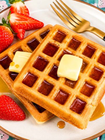 Golden homemade waffles with butter, maple syrup, and fresh strawberries