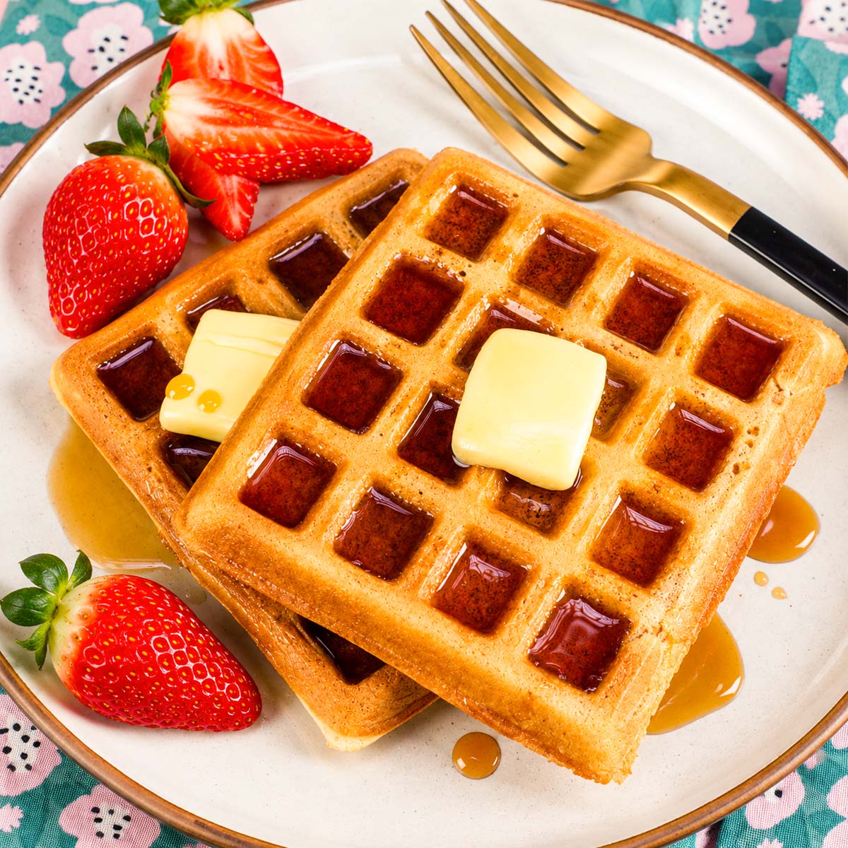Golden homemade waffles with butter, maple syrup, and fresh strawberries