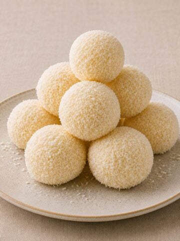 2 ingredient coconut balls coated in shredded coconut stacked on a speckled ceramic plate