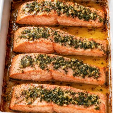 baked lemon dill salmon fillets in a white baking dish with garlic, fresh dill, and olive oil juices