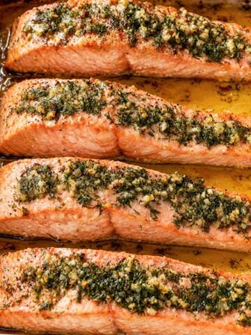 baked lemon dill salmon fillets in a white baking dish with garlic, fresh dill, and olive oil juices