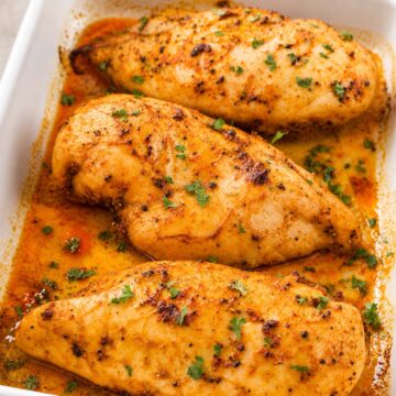 Juicy baked chicken breasts with paprika and herbs in a white baking dish