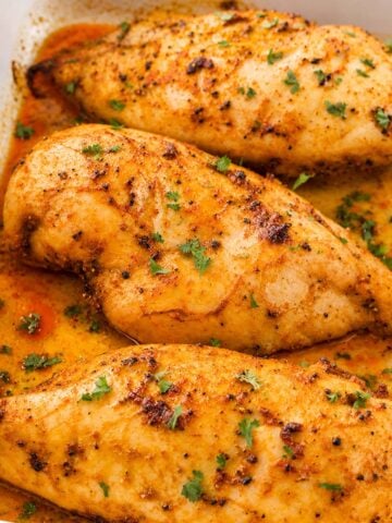 Juicy baked chicken breasts with paprika and herbs in a white baking dish