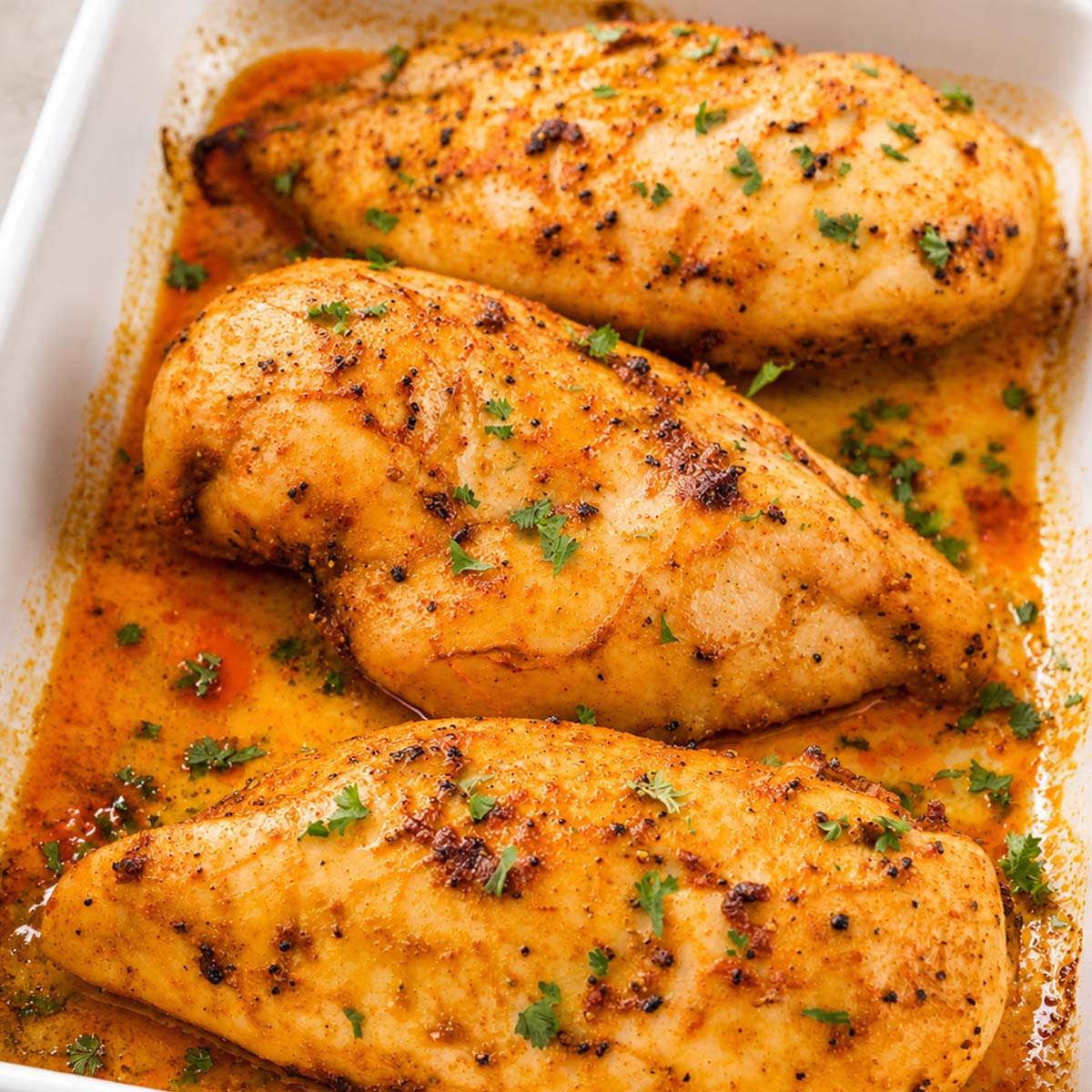Juicy baked chicken breasts with paprika and herbs in a white baking dish