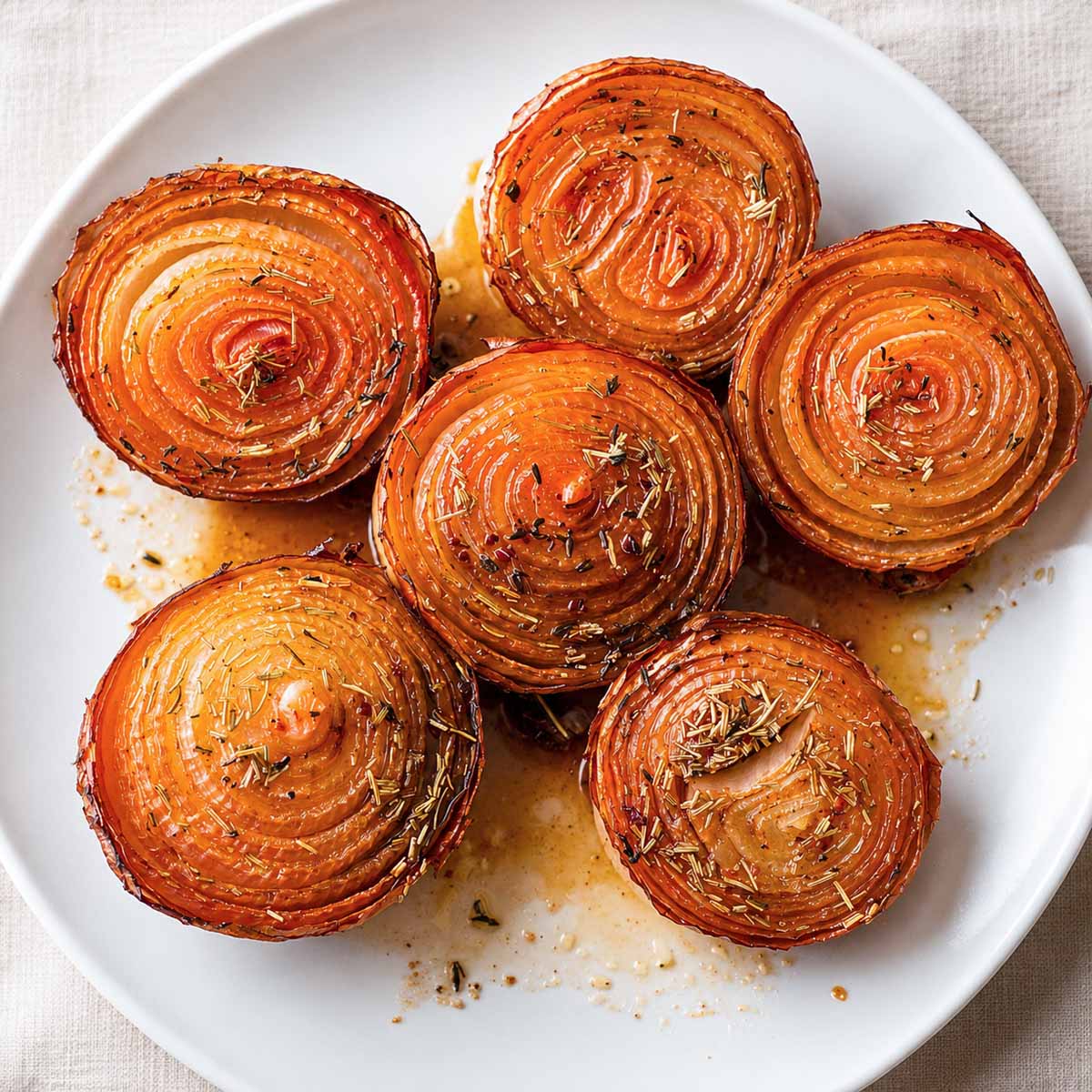 Balsamic roasted onions served on a white plate with caramelized layers and rosemary.