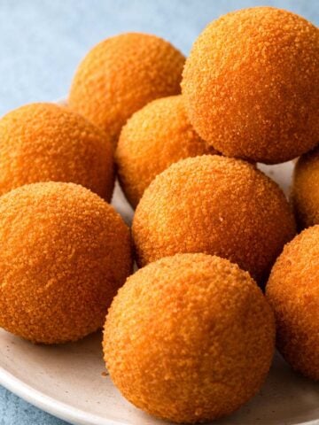 Golden, crispy chicken croquettes stacked on a white plate, showing their round shape and crunchy breadcrumb coating.