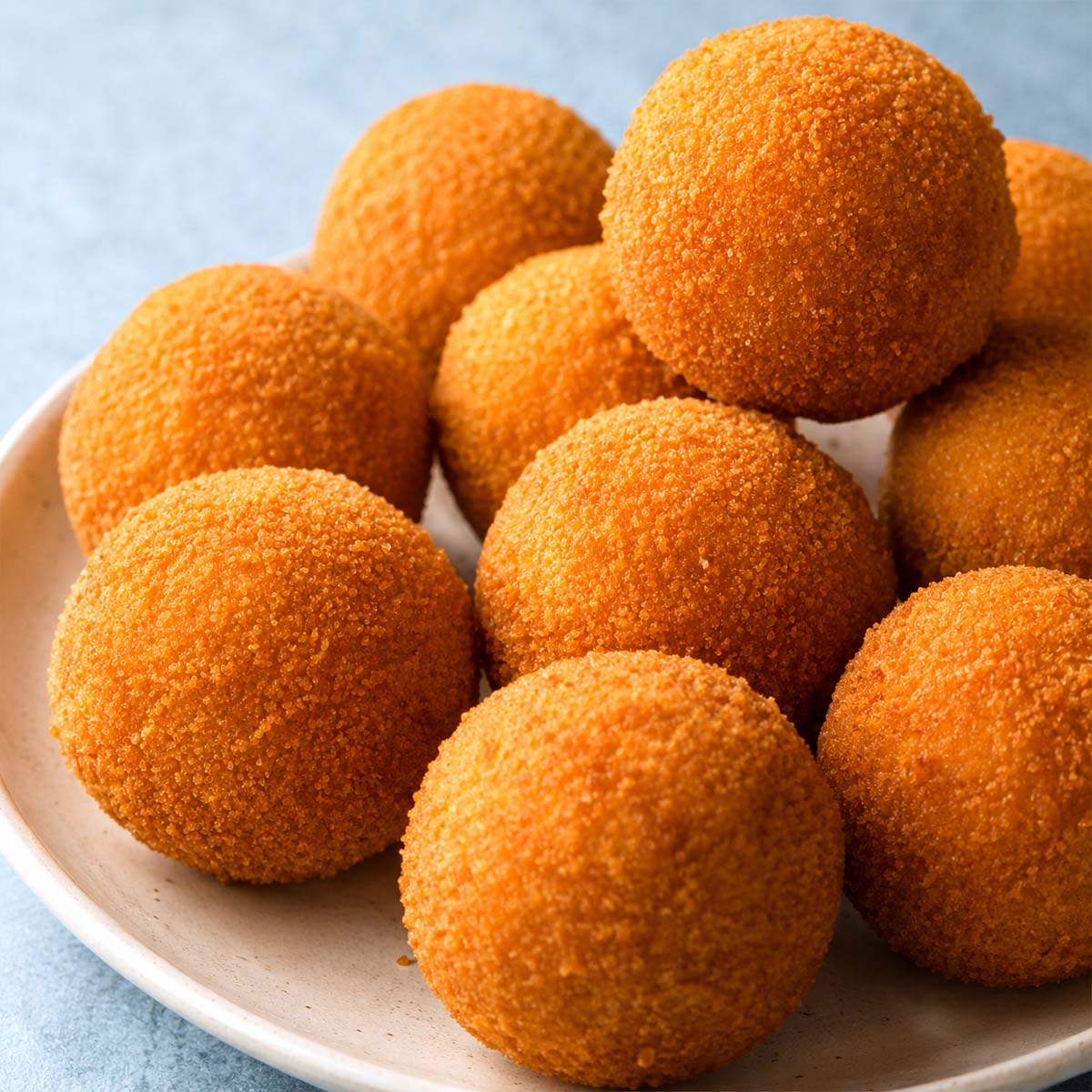 Golden, crispy chicken croquettes stacked on a white plate, showing their round shape and crunchy breadcrumb coating.
