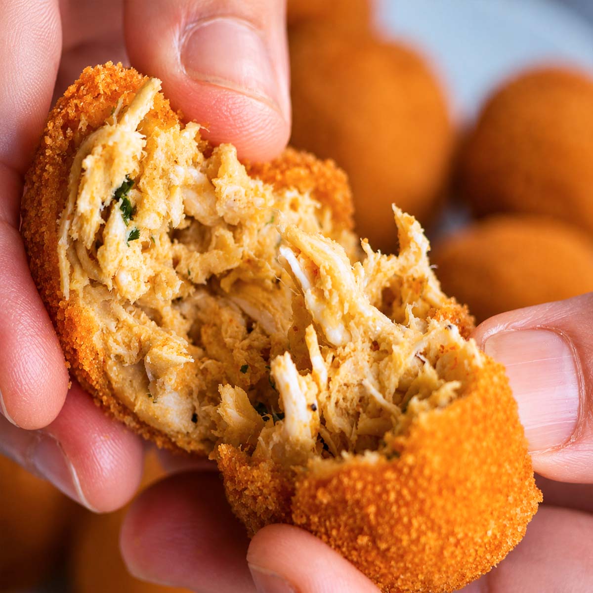 Close-up of a chicken croquette pulled open, showing its tender shredded chicken filling inside a crisp golden breadcrumb coating.