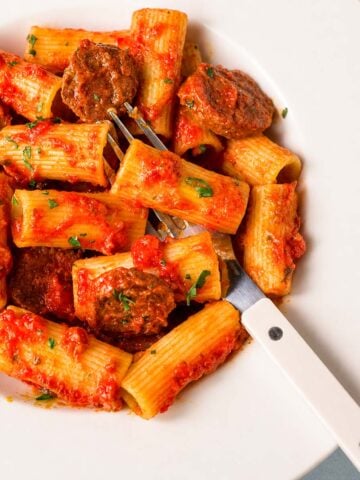 Fork lifting chorizo from Spanish chorizo pasta with tomato sauce