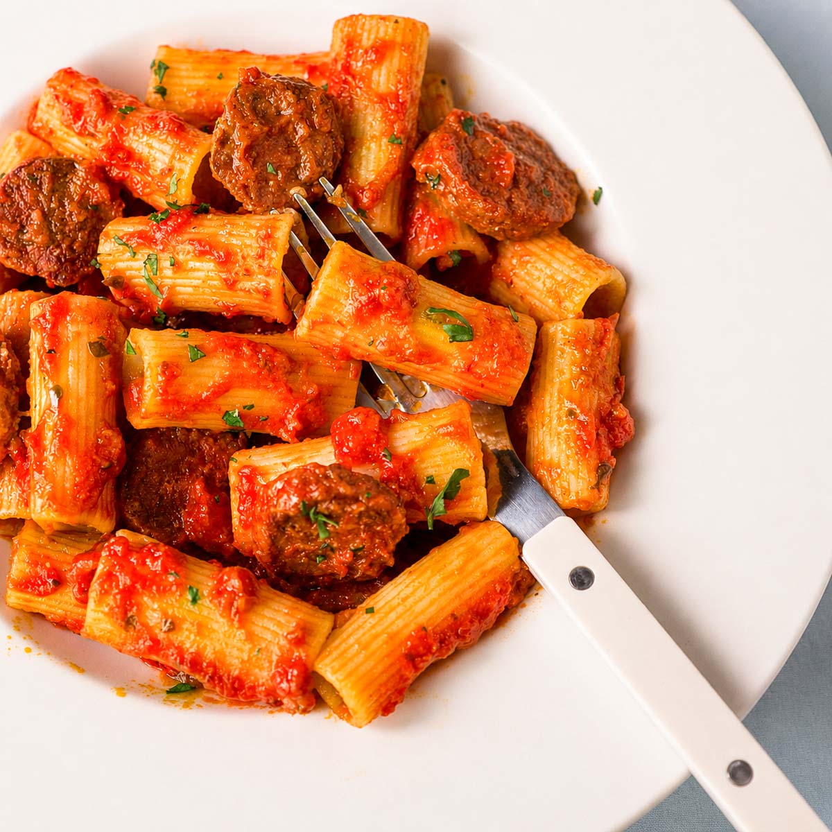 Fork lifting chorizo from Spanish chorizo pasta with tomato sauce