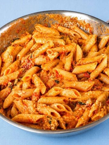 Creamy tomato penne pasta in a skillet with Parmesan cheese