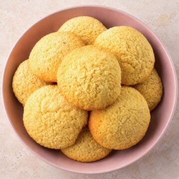 Easy coconut cookies piled in a pink bowl with golden edges and a soft, crumbly texture