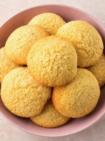 Easy coconut cookies piled in a pink bowl with golden edges and a soft, crumbly texture