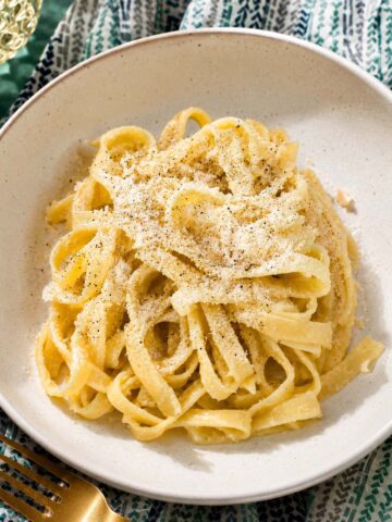Fettuccine al burro in a white bowl, coated in a creamy butter sauce and topped with grated Parmesan.