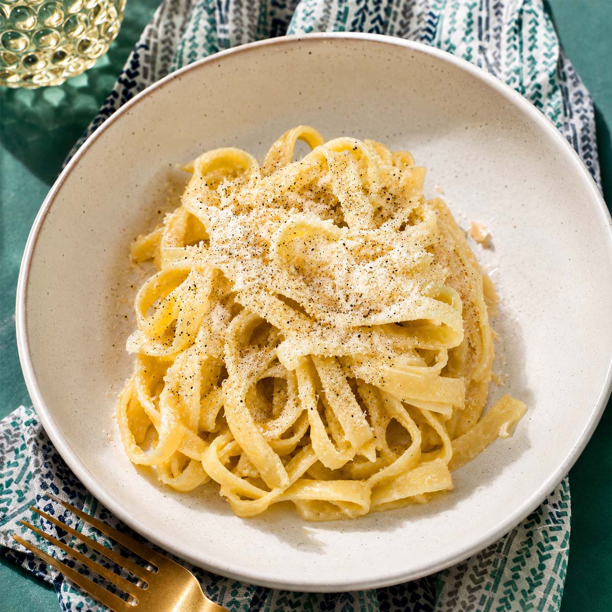 Fettuccine al burro in a white bowl, coated in a creamy butter sauce and topped with grated Parmesan. 