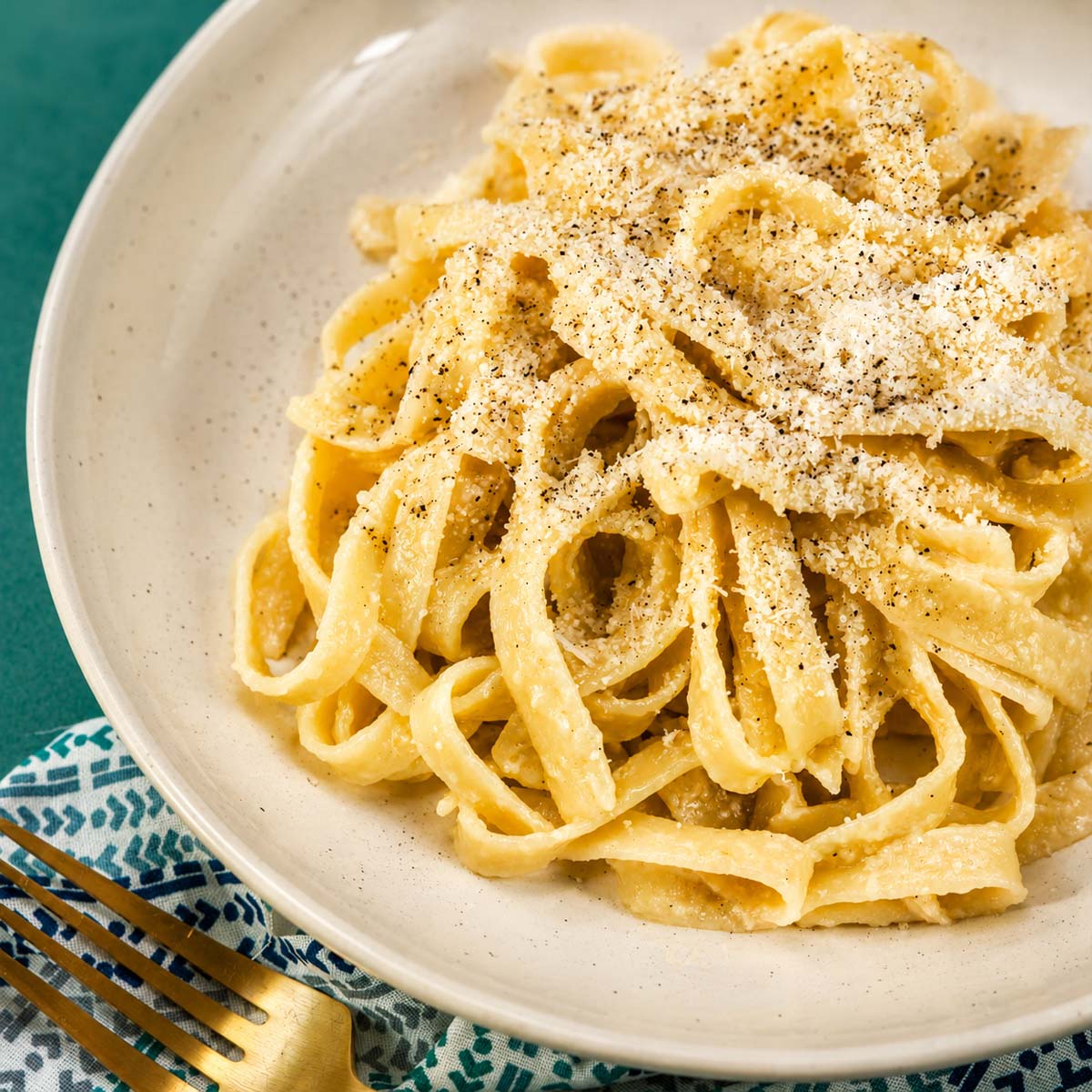 Close-up of fettuccine al burro in a white bowl, coated in buttery Parmesan sauce and finished with black pepper and grated cheese. 