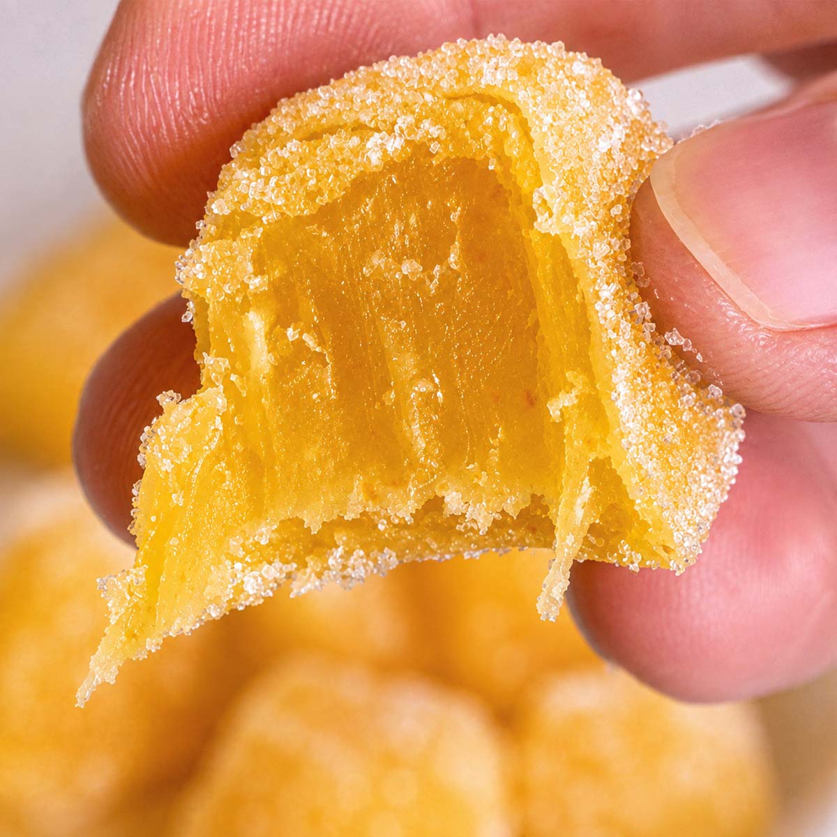 Close-up of a sugar-coated homemade fruit snack without gelatin, showing the soft, chewy orange gummy texture as it's held between fingers.