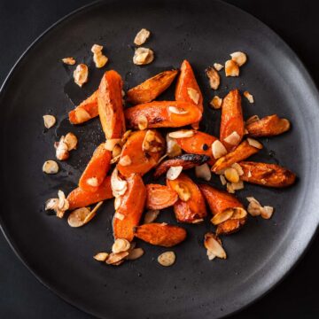 Honey roasted carrots with almonds served on a black plate, featuring caramelized honey glazed roasted carrots with toasted almonds.