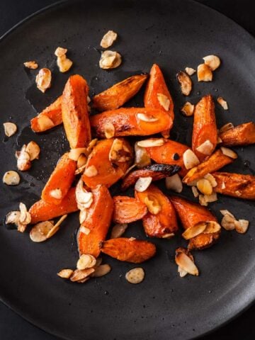 Honey roasted carrots with almonds served on a black plate, featuring caramelized honey glazed roasted carrots with toasted almonds.