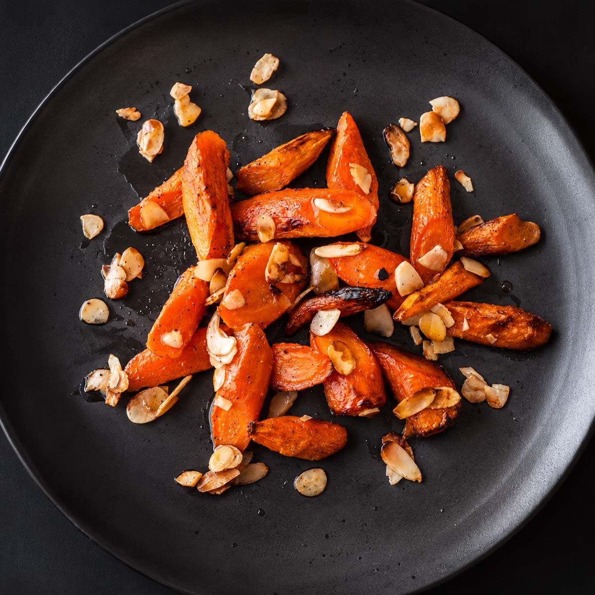 Honey roasted carrots with almonds served on a black plate, featuring caramelized honey glazed roasted carrots with toasted almonds.