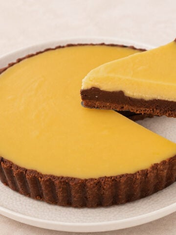 Chocolate orange tart with one slice lifted on a cake server, revealing its three distinct layers.