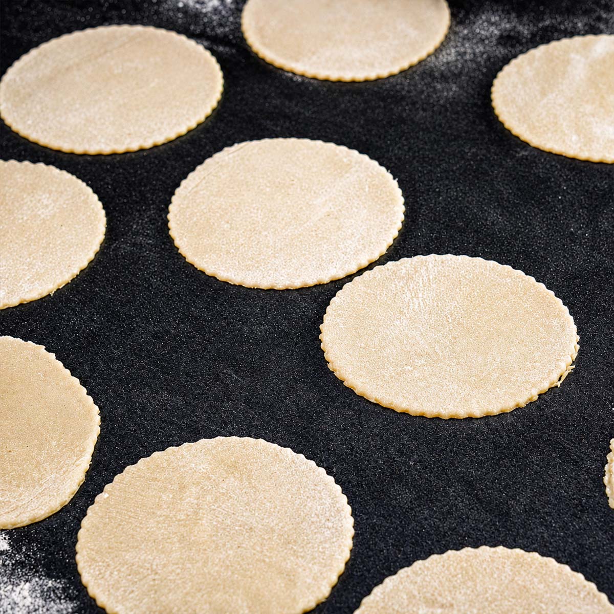 Pierogi dough circles cut from rolled dough and arranged on a lightly floured work surface.