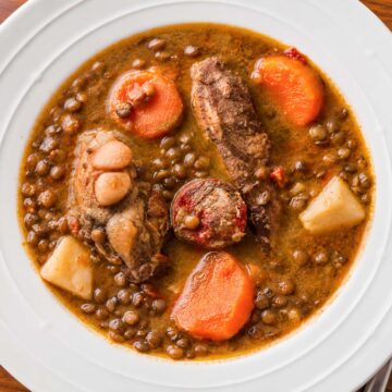 Spanish lentil stew with chorizo, pork ribs, potatoes, and carrots served in a white bowl