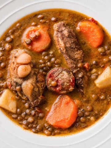 Spanish lentil stew with chorizo, pork ribs, potatoes, and carrots served in a white bowl