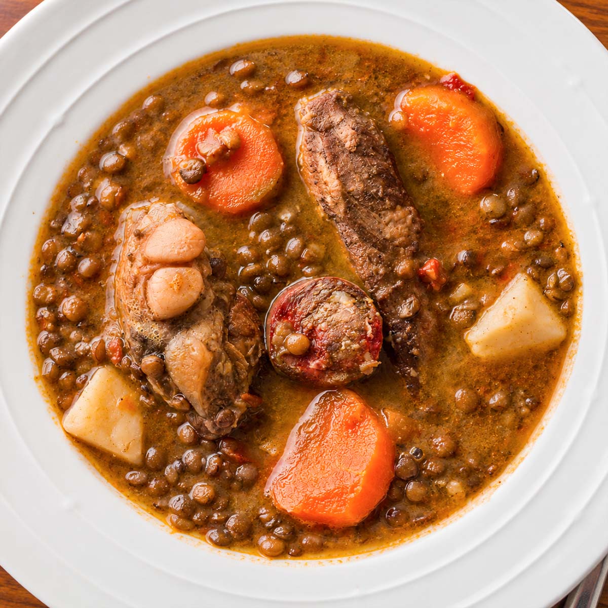 Spanish lentil stew with chorizo, pork ribs, potatoes, and carrots served in a white bowl