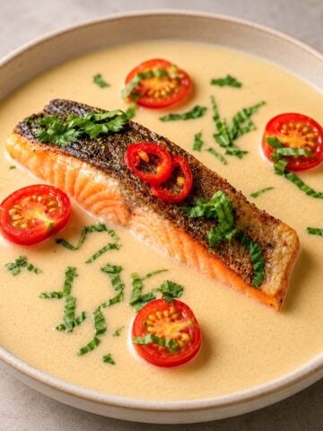 Pan-seared Thai coconut salmon in a creamy coconut sauce with cherry tomatoes, red chili and fresh herbs.