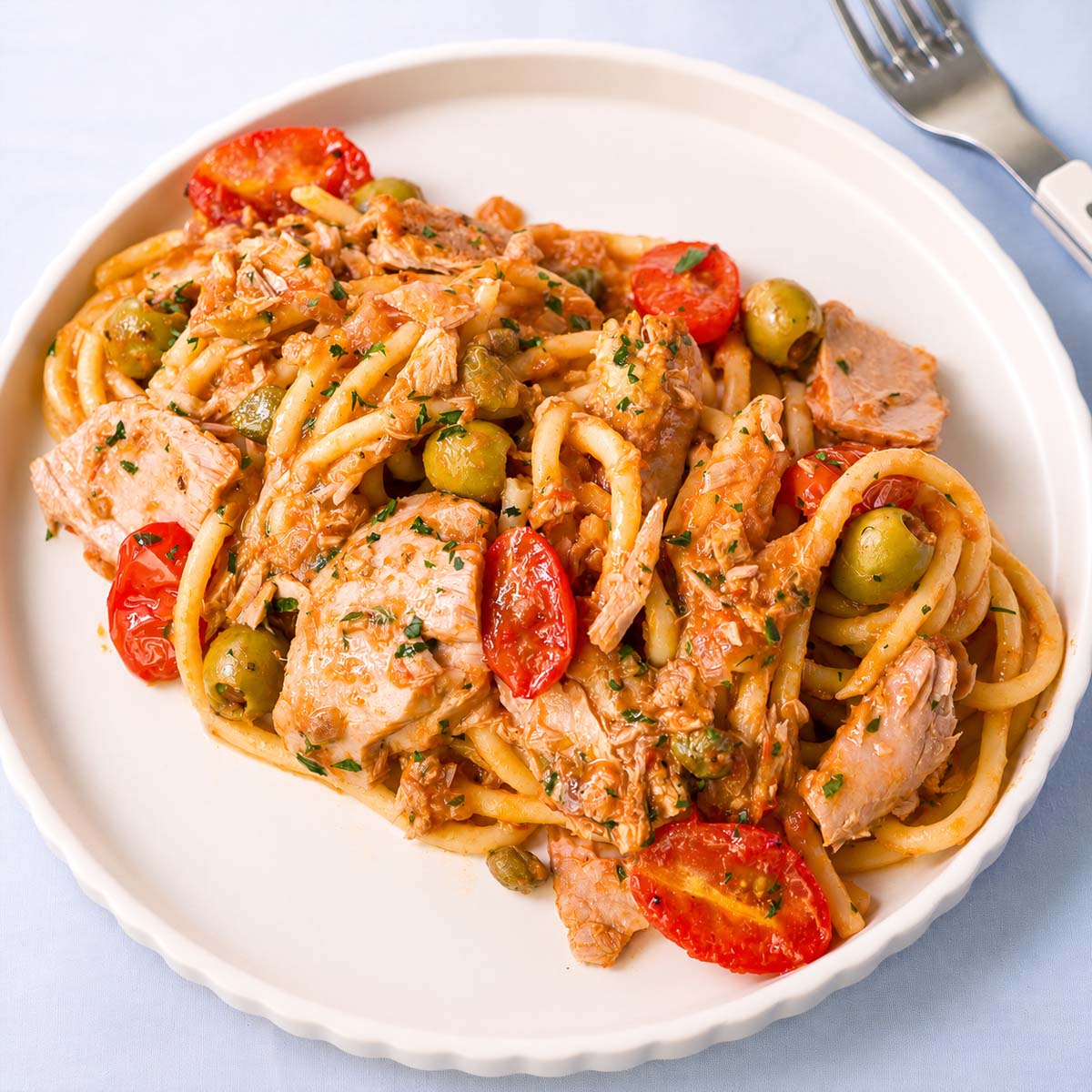 Tuna tomato pasta with green olives, cherry tomatoes, capers, and parsley in a tomato sauce