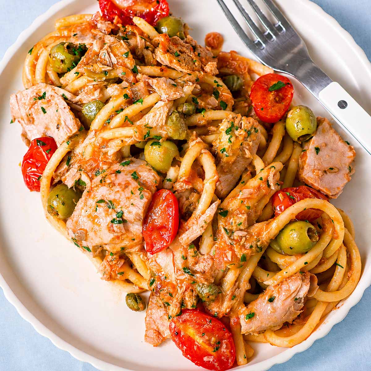 Close-up of tuna pasta with green olives, cherry tomatoes, capers, and chunky tuna